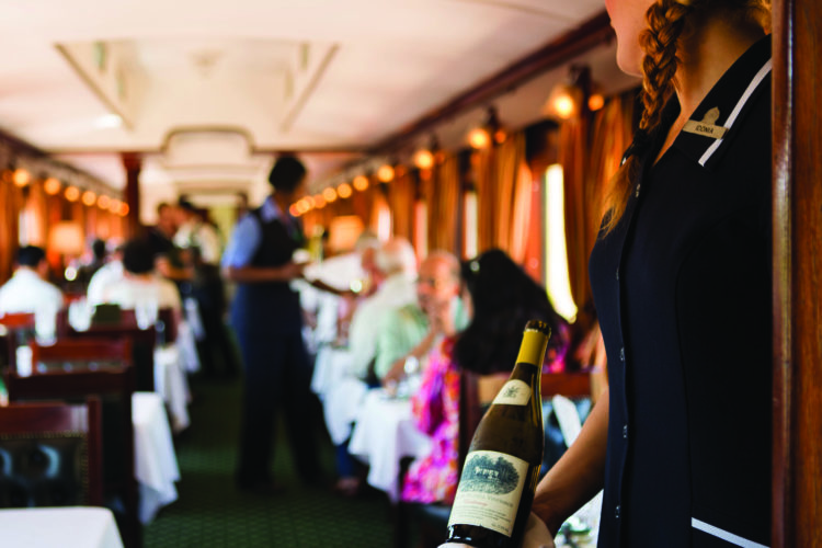 RVR-ServWineHostess-HRes Foto: Die Rovos Rail Fahrt können Sie mit einem Glas Champagner die atemberaubende Aussicht genießen.